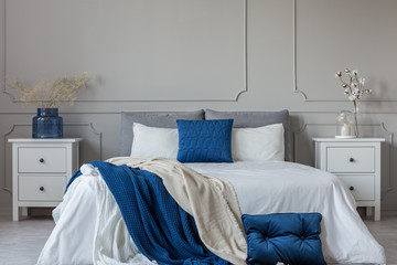 King size bed with grey, blue and white bedding between two wooden nightstands with flowers in vases