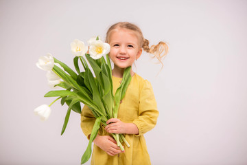 baby girl blonde with a bouquet of tulips on a light background.baby girl blonde smiling.spring and women's day concept.Cute little girl holding white tulips.copy spase
