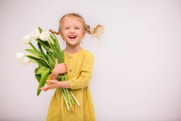 baby girl blonde with a bouquet of tulips on a light background.baby girl blonde smiling.spring and...