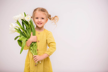 baby girl blonde with a bouquet of tulips on a light background.baby girl blonde smiling.spring and...