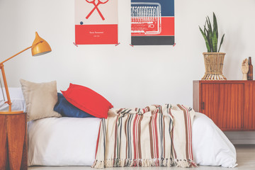 Real photo of a red and blue bedroom interior with a bed, lamp and posters