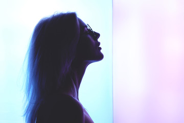 Profile of a beautiful young blond woman with glasses against a background of blue pink creative neon lighting
