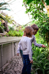 The boy and girl searching beautiful tropical herbs in glass botanical garden in winter. Botanical green garden full of greenery. Happy, bright, modern, colorful, vertical