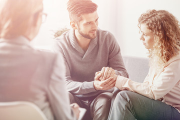 Bright photo of handsome husband apologizing his worried wife during couple therapy with psychotherapist