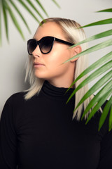 Profile of beautiful woman with sunglasses hiding behind tropical palm leaves