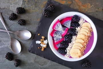 Healthy blackberry smoothie bowl with coconut, bananas, dragon fruit and granola. Top view table...