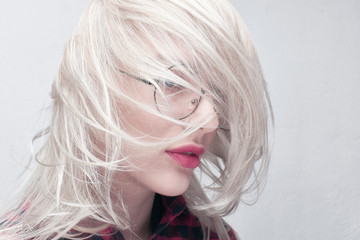 Portrait of a young beautiful blonde woman in round glasses and with plump lips in a red checkered...