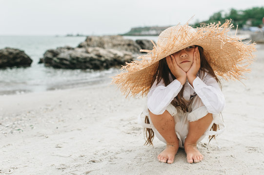 Adorable little girl in straw hat at beach during summer vacation