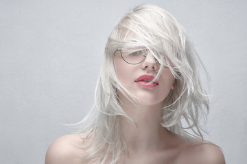 Portrait of a young beautiful blonde woman in round glasses and with plump red lips with bare shoulders on a white background. Fashionable fancy hairstyle