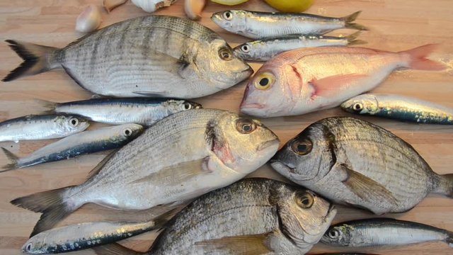 Fresh fish with lemon ready for cooking. Preparing delicious and tasty seafood meal. Uncooked Gilt-head sea bream, Sardines, Common pandora, top view. Healthy food concept. Raw fish. Cooking dinner