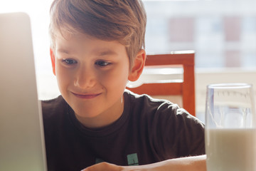 Happy young boy at home using a laptop to do his homework