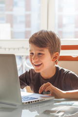 Happy young boy at home using a laptop to do his homework