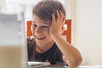 Happy young boy at home using a laptop to do his homework