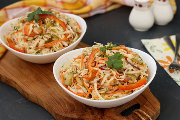 Healthy salad from cabbage, sweet pepper, onion and orzo pasta is located in a white bowl on a wooden board