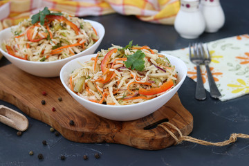 Healthy salad from cabbage, sweet pepper, onion and orzo pasta is located in a white bowl on a wooden board
