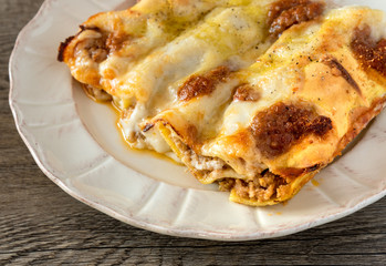 Cannelloni, Italian pasta pastry tubes stuffed with mince meat with white bechamel sauce and cheese crust, in the plate on the old wooden background.
