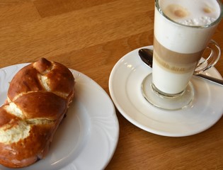 glass of latte macchiato and a wicker bun on a white saucer