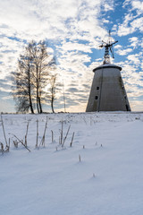 Empty Countryside Landscape in Sunny Winter Day with Snow Covering the Ground with Big Abandoned Windmill in Background