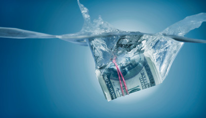 Money concept. Rolled American US Dollars banknotes sinking in water as symbol of global financiall crisis and uncertain future of international trade and investment.