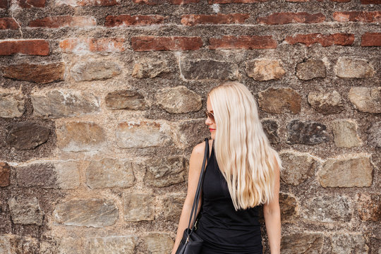 Woman with blond hair wearing sunglasses while standing against old wall