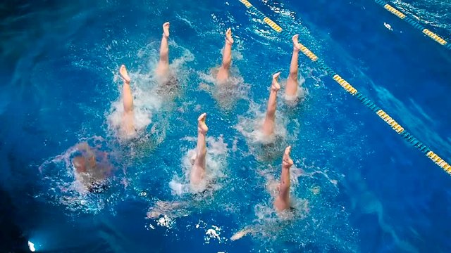 Synchronized swimming. Young girls learn swimming in the pool. Young girls are trained to competitive swimming in the pool. Water team sports, girls synchronized swimming