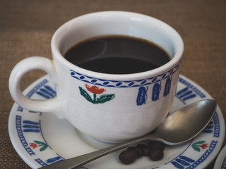 Breakfast of a porcelain coffee cup, an antique spoon and coffee beans on a vintage burlap background