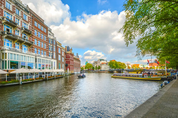 A small boat glides past tourist boats on a large canal near the museum district of Amsterdam in early Autumn.
