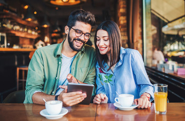 Young couple having fun with tablet in a cafe. Dating, relationships, love, romance, lifestyle, technology