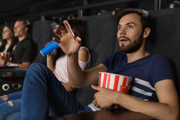 Shocked bearded man keeping popcorn in hands and carefully watching new interesting film at cinema. Excited viewer expecting final of intriguing movies. Concept of entertainment and interest.
