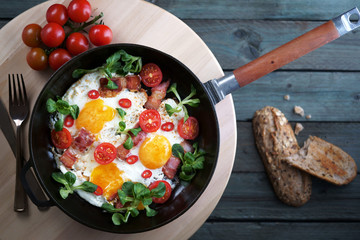 fried eggs with bacon tomatoes and greens, cast iron pan, top view