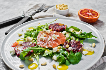 Healthy salad with arugula, grapefruit, red oranges, nuts and tofu cheese. Gray background, side view