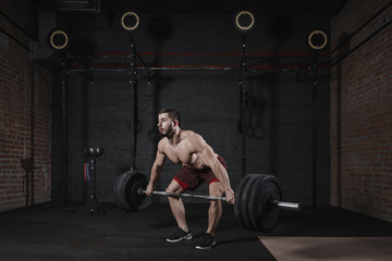 Fototapeta na wymiar Young shirtless athlete lifting heavy barbell at crossfit gym. Handsome man practicing powerlifting deadlift exercise.