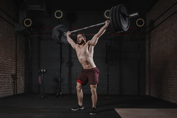 Crossfit athlete lifting barbell overhead at the gym. Shirtless man doing functional training. Practicing powerlifting.