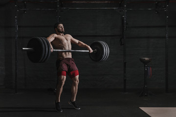 Fototapeta na wymiar Muscular man lifting a barbell in crossfit gym.