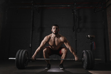 Fototapeta na wymiar Young crossfit athlete lifting barbell at gym. Muscular shirtless man doing functional training. Deadlift exercise.
