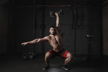 Crossfit athlete doing overhead dumbbell squats at the gym. Handsome man doing functional training. Practicing workout