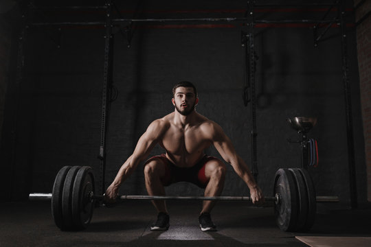 Young crossfit athlete lifting barbell at gym. Muscular shirtless man doing functional training. Deadlift exercise.