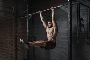 Crossfit athlete doing abs exercise on horizontal bar at the gym. Handsome man doing functional training workout. Practicing calisthenics. - obrazy, fototapety, plakaty