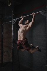 Young crossfit athlete doing pull-ups at the gym. Handsome man doing functional training....