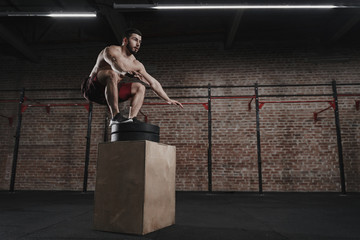 Crossfit athlete is performing box jump at gym. Handsome man doing functional training. Workout exercises. Copy space