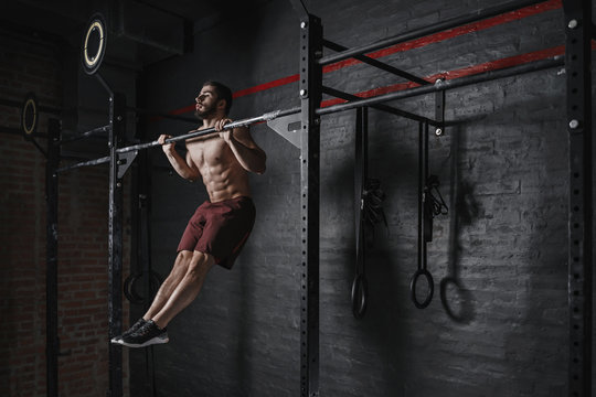 Crossfit athlete doing pull-ups at the gym. Practicing calisthenics.  Handsome man doing functional training. Photos | Adobe Stock