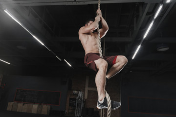 Crossfit athlete climbing a rope at the gym. Handsome man doing functional training. Workout exercises