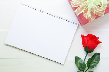 Present gift with red rose flower and notebook with copy space on wooden table, 14 February of love day with romantic, valentine holiday concept.