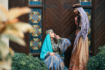 Women in traditional Azerbaijani dress knocking the wooden door of an old house