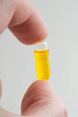 Fingers holding 3d vitamin D capsule with blank background.
