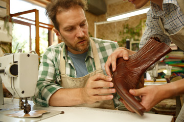 Senior bearded tailor, carefully looking at brown leather boot.