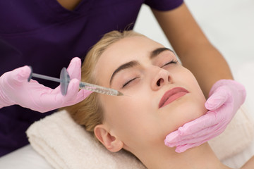 Closeup of woman face with closed eyes lying on couch during lifting procedure in spa salon. Attractive blonde caring about her face skin and receiving injection. Concept of beauty.