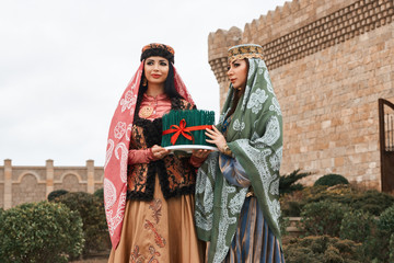 Two women in national clothes holding sprouts of spring wheat grass semeni for Novruz holiday