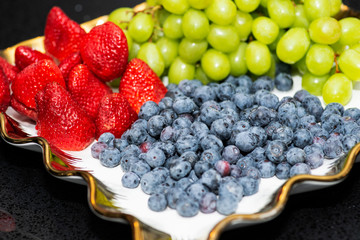 Fresh fruit platter with arranged organic blueberries, strawberries, grapes on banquet table at business or wedding event venue.