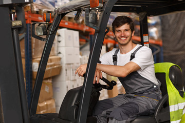 Good looking loader sitting in forklift, posing and smiling. Professional worker wearing uniform...